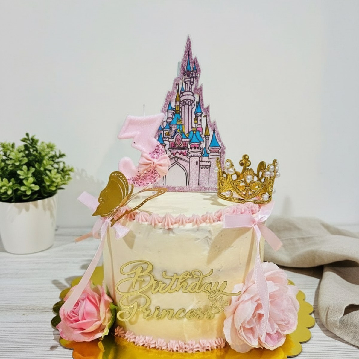 Gâteau d’anniversaire blanc et rose sur le thème princesse Disney, avec château, couronne, papillon doré et topper Birthday Princess